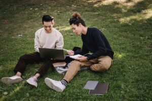 High angle full body of diverse classmates using laptop for homework assignment while sitting on grass in park