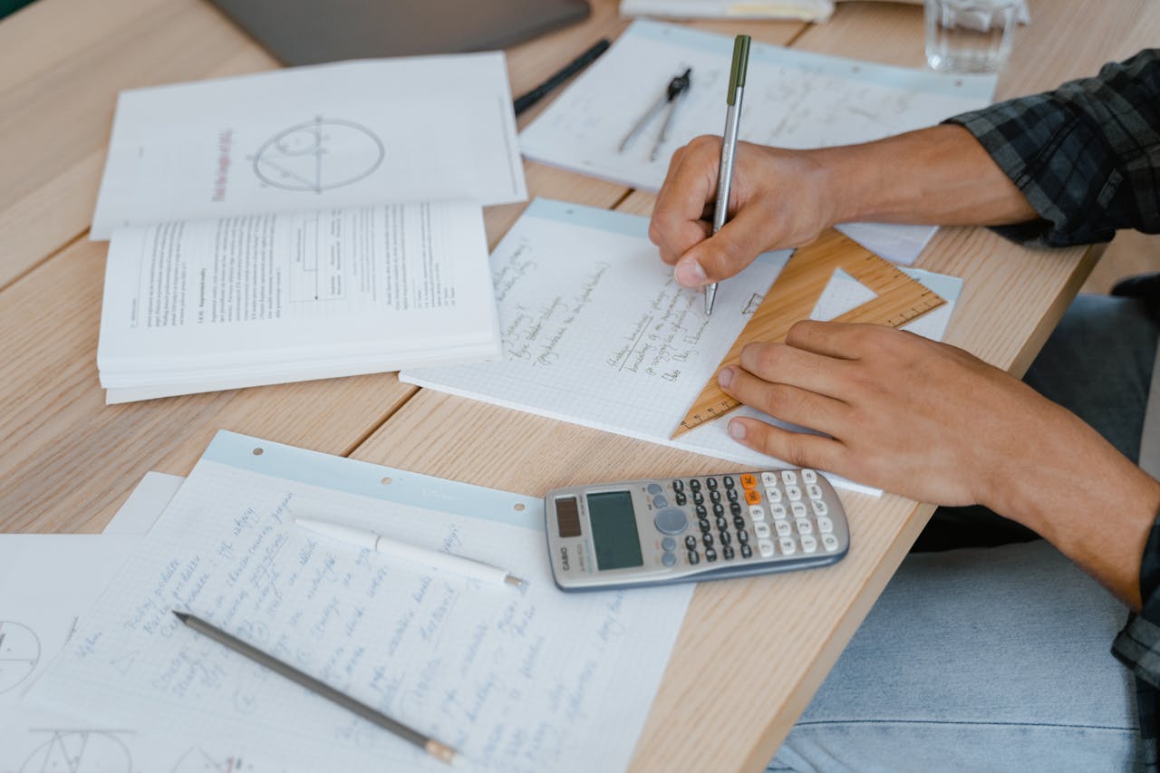 A student engaged in solving math problems using a calculator and stationery on a desk.